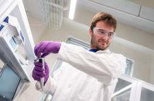 A man wearing a white lab coat, safety glasses and purple gloves works in a catalysis engineering research lab.